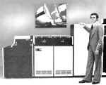 A man stands in front of a RP20 disk drive, while a picture of a sailboat (the unofficial LCG emblem) hangs prominently on the wall.